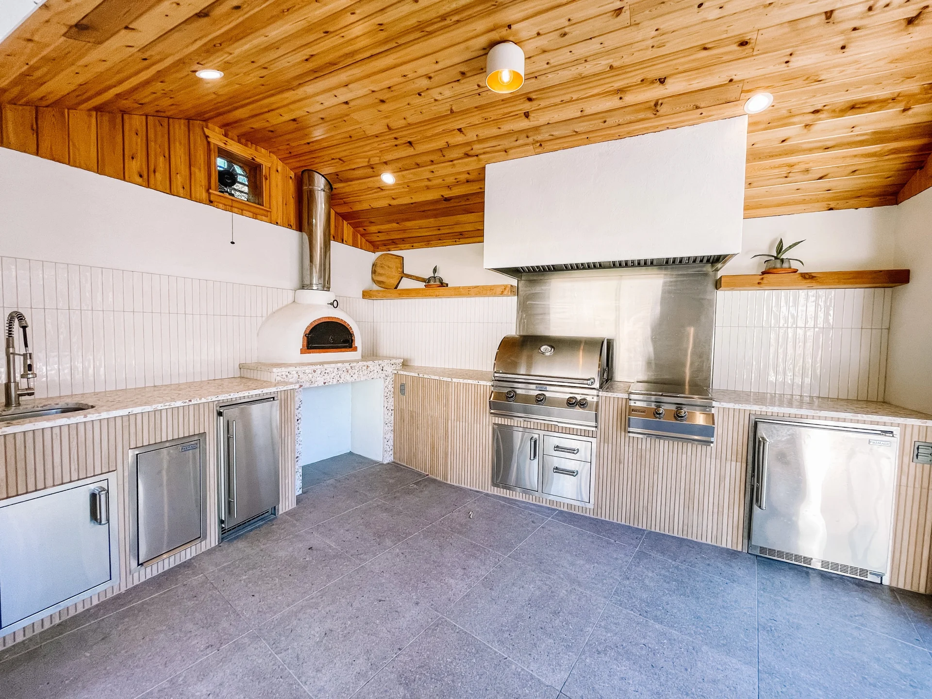 Finished outdoor kitchen with stainless steel grill, white cabinetry and a natural wood ceiling