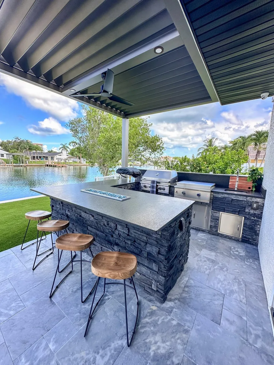 Outdoor kitchen with dark stone island, wood stools and pergola