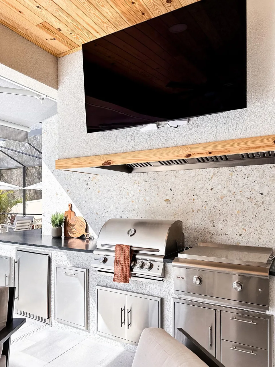Built-in stainless steel grill beneath a television and wood ceiling